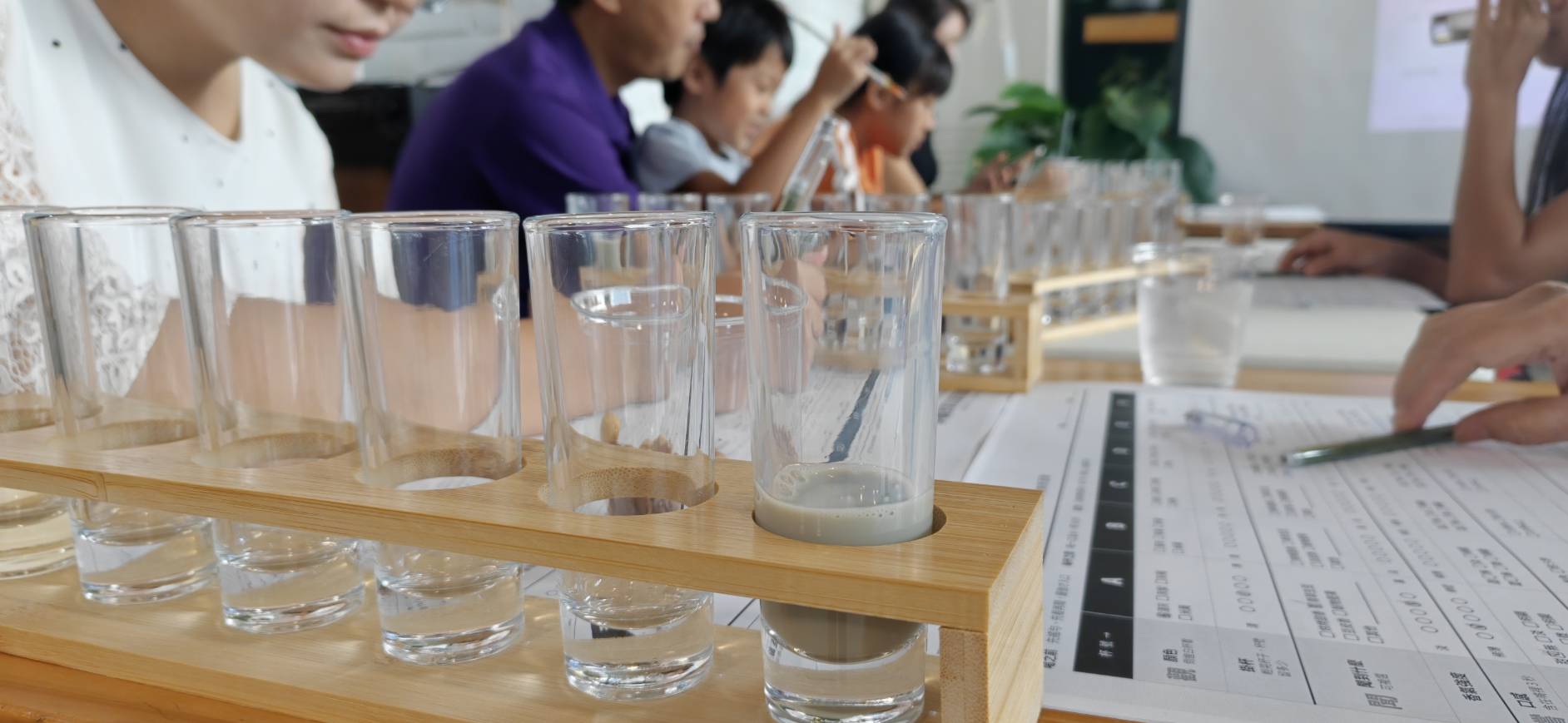 竹製品飲架上的六杯無標籤黑豆漿與盲飲記錄卡