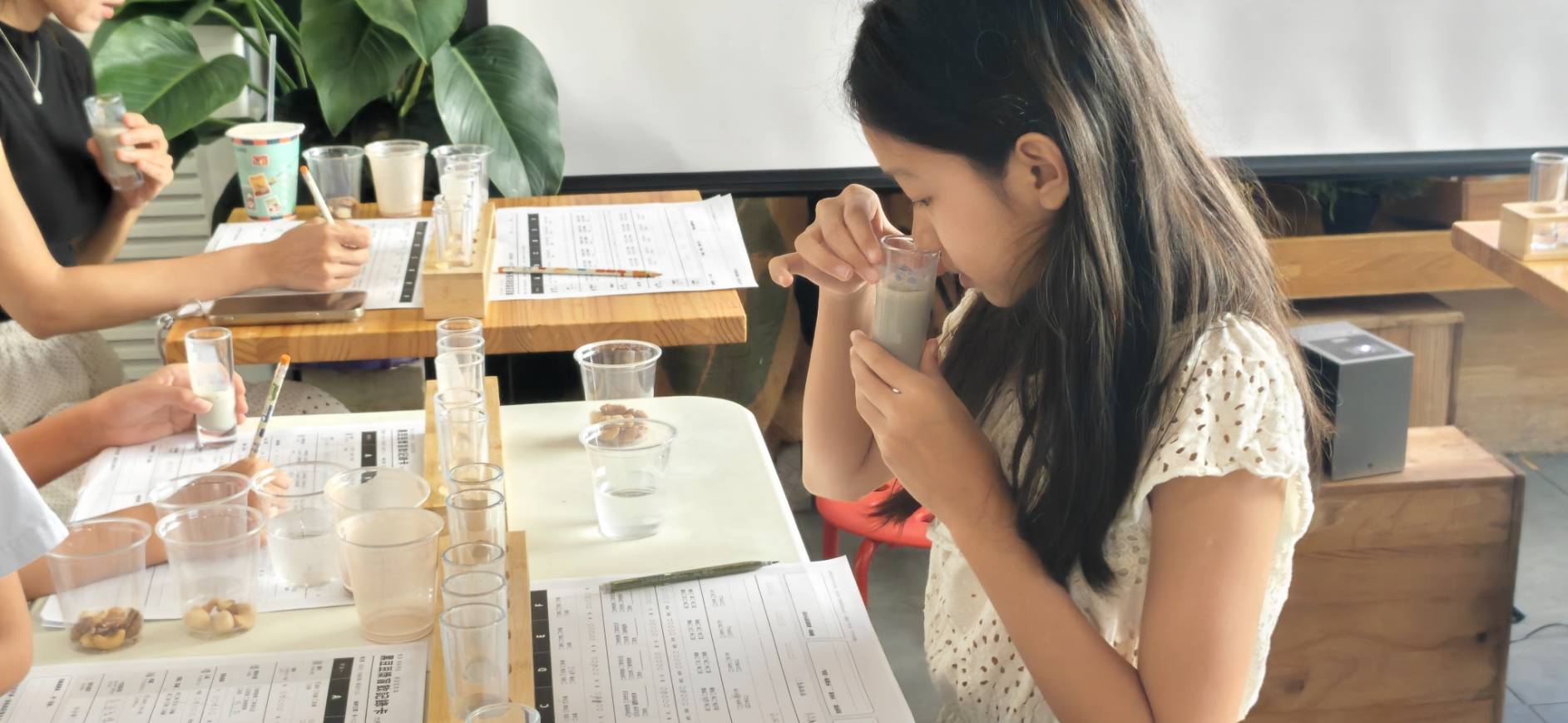 小學員低頭聞黑豆漿的香氣,桌上擺著六杯盲飲與品飲記錄卡
